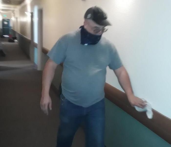 man in mask walking through hallway cleaning wall with cloth